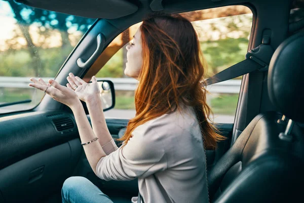 Feliz mulher ruiva em um casaco bege no banco da frente de um modelo de sorriso de carro gesticulando com as mãos companheiro de viagem — Fotografia de Stock