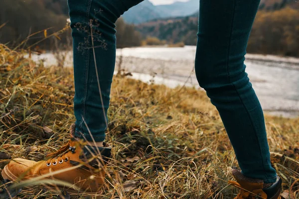 Damenfüße Jeans Schuhe trockenes Gras Herbst Flussberge in der Ferne — Stockfoto