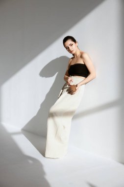 Duvarın yanında beyaz pantolonlu esmer bir kadının portresi ve düşen bir gölge.