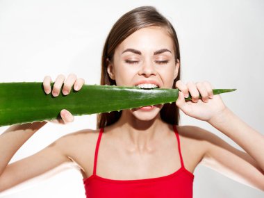 Beyaz dişli, aloe yaprağı ısıran ve kırmızı tişörtlü bir kadın.