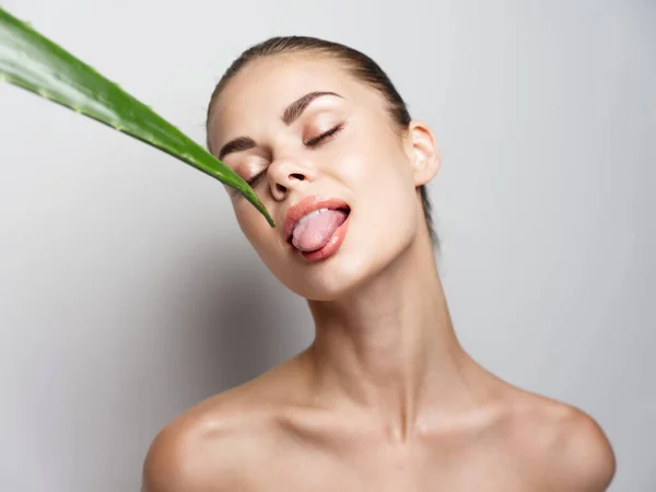 Mulher com olhos fechados toca uma folha de aloés verde com a língua em um fundo leve — Fotografia de Stock