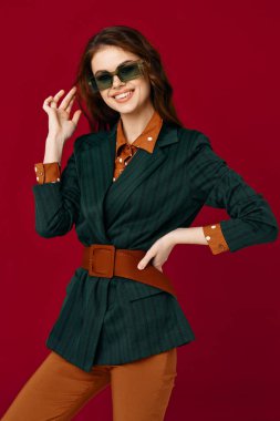 Güneş gözlüğü takan, el hareketleriyle hareket eden kırmızı arka planı olan bir kadın.