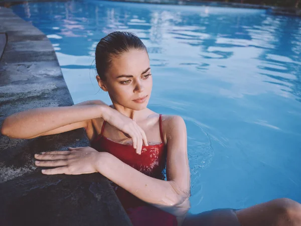 Uma mulher de fato de banho vermelho senta-se na piscina com os cotovelos na telha com as mãos — Fotografia de Stock
