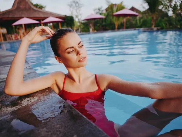 Donna in costume da bagno rosso tocca la testa con la mano e nuota in piscina in estate nella natura — Foto Stock