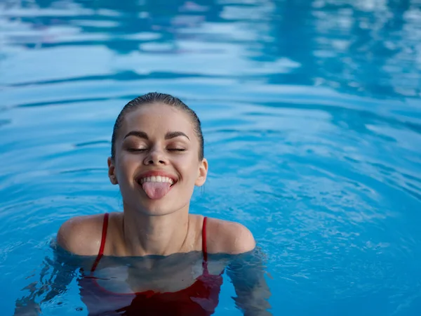 Веселая женщина в бассейне в красном купальнике показывает языковой отдых — стоковое фото