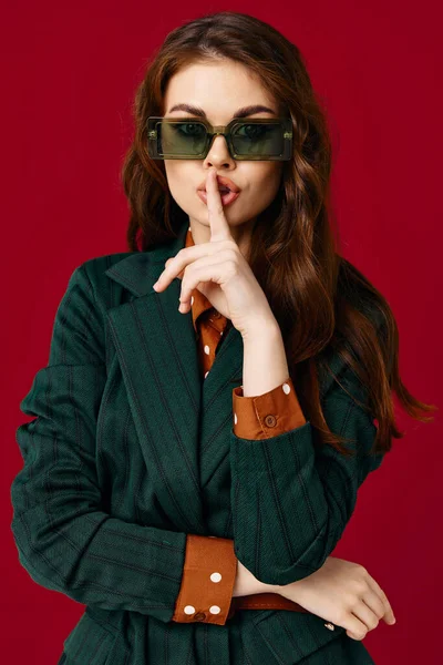 Brunetka nosi okulary przeciwsłoneczne trzyma rękę w pobliżu twarzy luksusowe czerwone tło — Zdjęcie stockowe