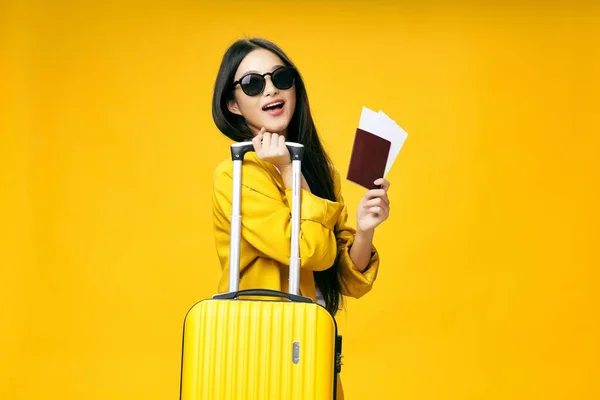 Woman with suitcase passport and plane ticket vacation yellow background — Stock Photo, Image