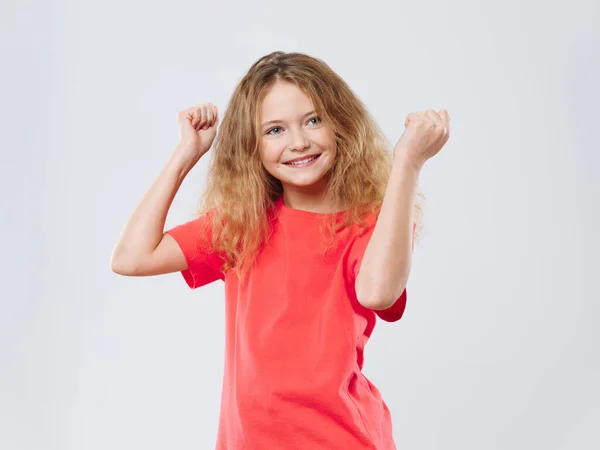 빨간 티셔츠를 입은 행복 한 곱슬머리 소녀가 가벼운 배경에서 신나는 즐거운 감정으로 춤을 추고 있다 — 스톡 사진