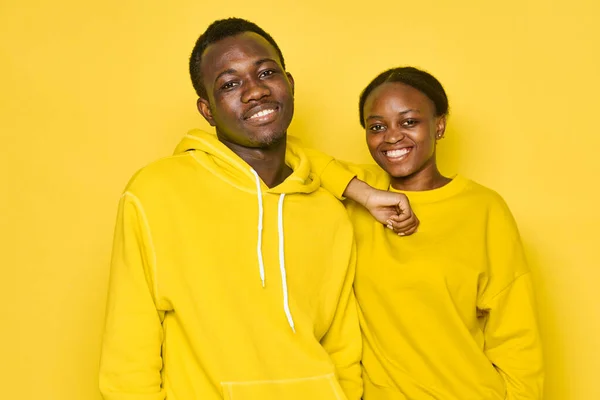 Happy man and woman of African appearance in identical sweaters on a yellow background laugh and — Photo