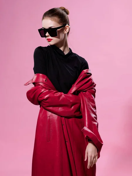 Mooie vrouw dragen zonnebril lederen jas mode roze achtergrond — Stockfoto