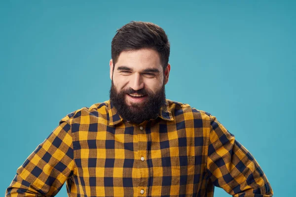 A man with a beard and a plaid shirt holds his hands on his belt on a blue background — Stock Photo, Image