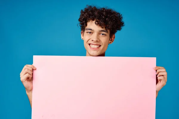 Homme aux cheveux bouclés tenant affiche rose bannière fond bleu — Photo
