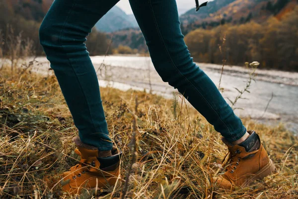 Damenfüße Jeans Schuhe trockenes Gras Herbst Flussberge in der Ferne — Stockfoto
