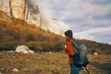 Sonbaharda sırt çantalı güzel bir kadın dağlarda kot pantolon giyiyor.