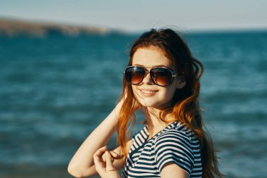 Deniz kenarındaki dağlarda güneş gözlüklü kızıl saçlı bir kadının portresi ve kahkahalar atan bir seyahat. 