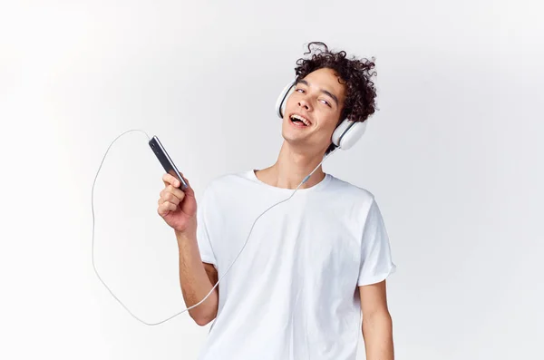 Bouclé gars dans les écouteurs avec un téléphone dans ses mains technologie de la musique — Photo