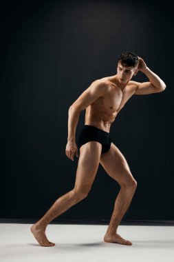 Siyah külotlu, şişirilmiş çıplak bir vücudu olan seksi bir adam karanlık bir arka plana karşı poz veriyor.