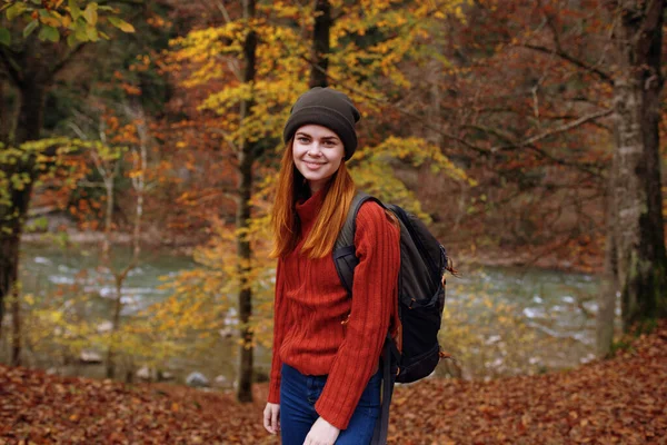 Ormanda sonbaharda uzun ağaçların yanında sırt çantalı kazaklı bir kadın turist. — Stok fotoğraf
