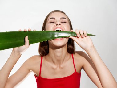 Yüzünün yanında aloe yaprağı olan temiz cilt kozmetolojisi olan kırmızı tişörtlü çıplak bir kadın.