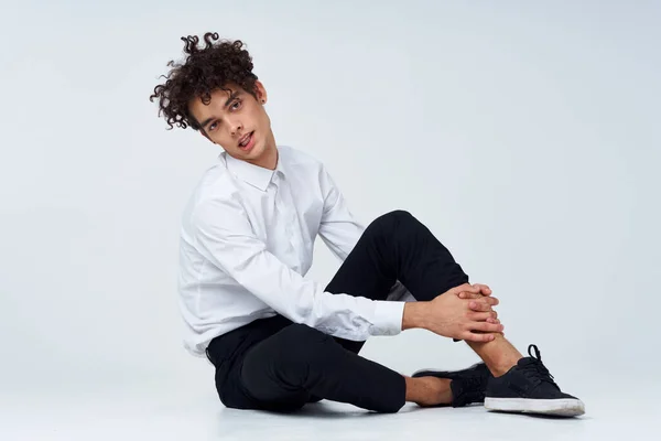 Trendy guy with curly hair in a classic suit and sneakers on the floor indoors photography studio — Stock Photo, Image