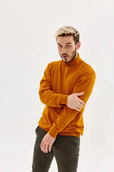 Hombre rubio de moda en un suéter naranja y pantalones sobre un fondo claro —  Fotos de Stock