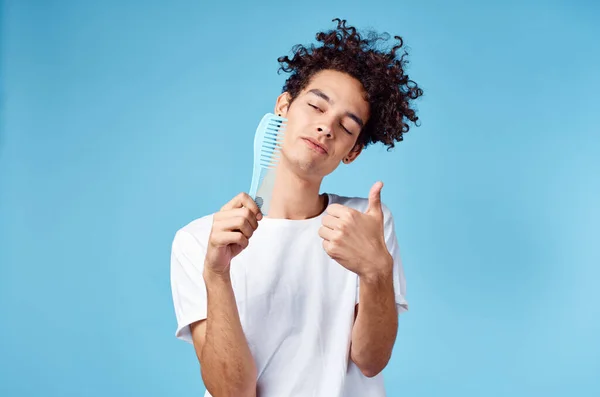 Homem emocional com um pente na mão e cabelos cacheados em um fundo azul Espaço Copiar — Fotografia de Stock