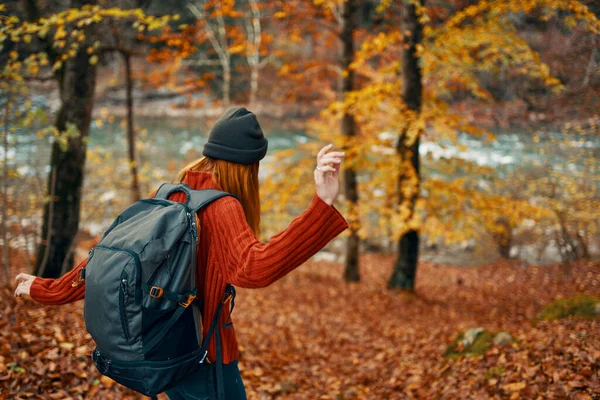 Escursionista donna con zaino nella foresta autunnale vicino al fiume di montagna e foglie cadute — Foto Stock