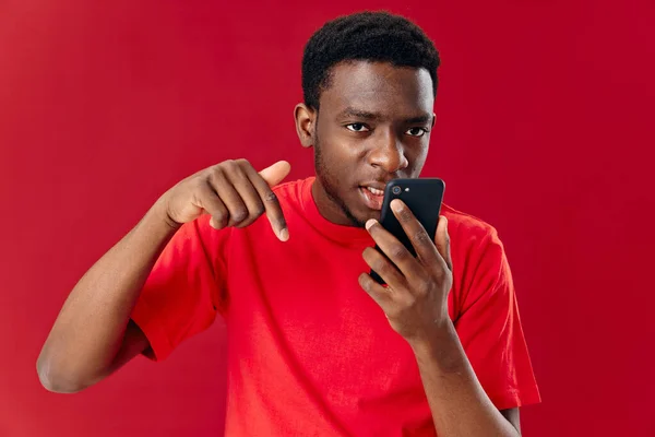 Hombre de apariencia africana en una camiseta roja con un teléfono en manos de la tecnología de la comunicación — Foto de Stock