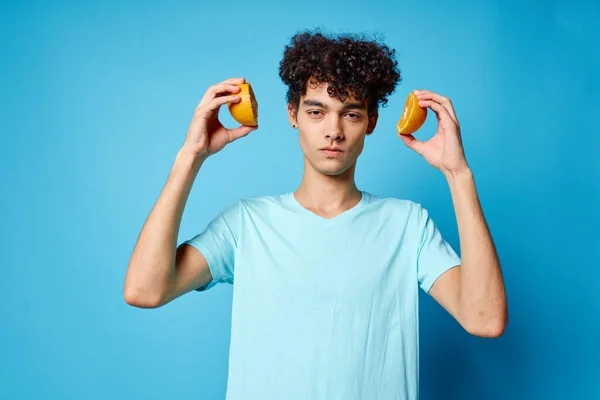 Man met krullend haar sinaasappels met fruit studio blauwe achtergrond — Stockfoto