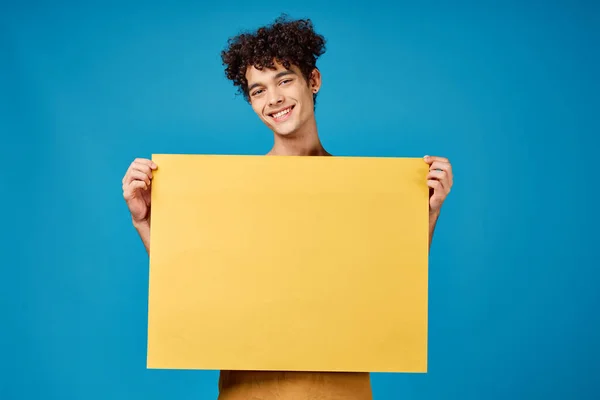 Homme joyeux avec poster jaune maquette bleu fond studio — Photo