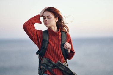 Kadın yürüyüşçü, deniz kenarında bir sırt çantasıyla doğa dağlarında ve kırmızı bir süveter mankeni.