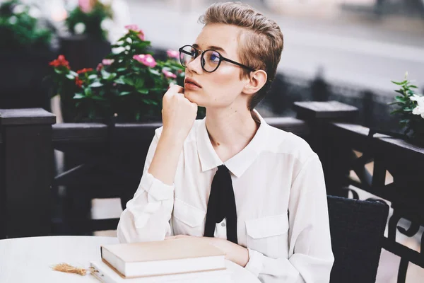 穿着衬衫和眼镜的年轻女子，带着一本书坐在餐馆的桌子旁 — 图库照片