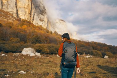 Sonbaharda sırt çantalı güzel bir kadın dağlarda kot pantolon giyiyor.