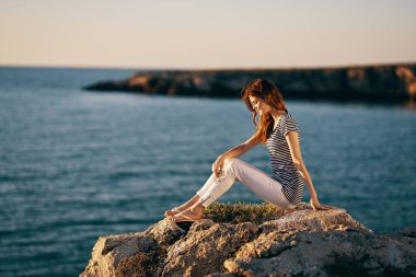 Kadın deniz kıyısında büyük taştan bir deniz manzarasında gün batımında.