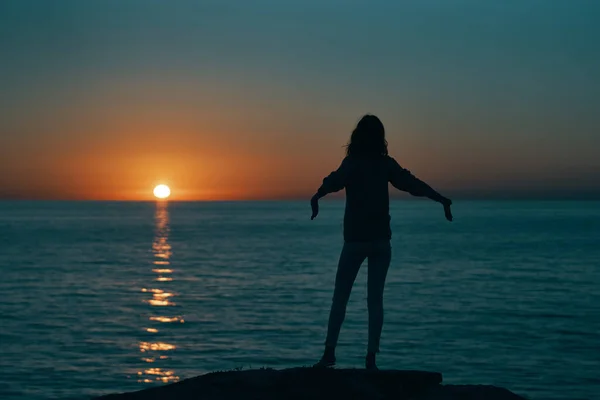 一个女人在日落时在大海边的轮廓，手拿着后视镜 — 图库照片