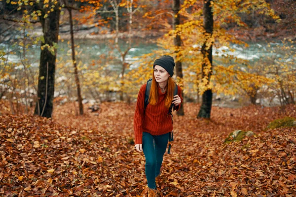 Turystka podróżująca w swetrze i dżinsach w jesiennym lesie w pobliżu górskiej rzeki — Zdjęcie stockowe