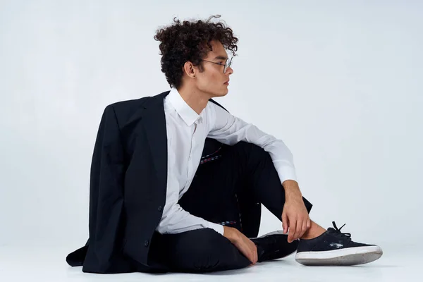 Κομψό άνδρα με σγουρά μαλλιά σε sneakers σε ελαφρύ φόντο ένα σακάκι στον ώμο παντελόνι μοντέλο — Φωτογραφία Αρχείου