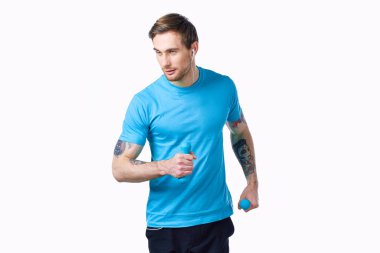 Kolunda mavi tişörtlü ve kaslı vücut geliştirme formundaki dövmeli bir adam.