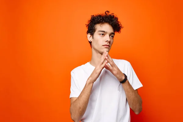 Lockig kille i en vit t-shirt gester med handen på en orange bakgrund — Stockfoto
