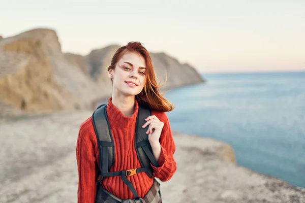 Donna in un maglione con uno zaino sulla schiena vicino al mare in montagna sorridere modello divertente — Foto Stock