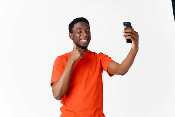 Cara feliz de aparência africana em uma camiseta laranja com um telefone celular — Fotografia de Stock