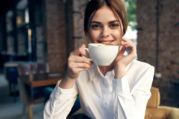 흰색 셔츠를 입은 예쁜 사업가가 커피를 마시며 카페에 앉아 있습니다 — 스톡 사진