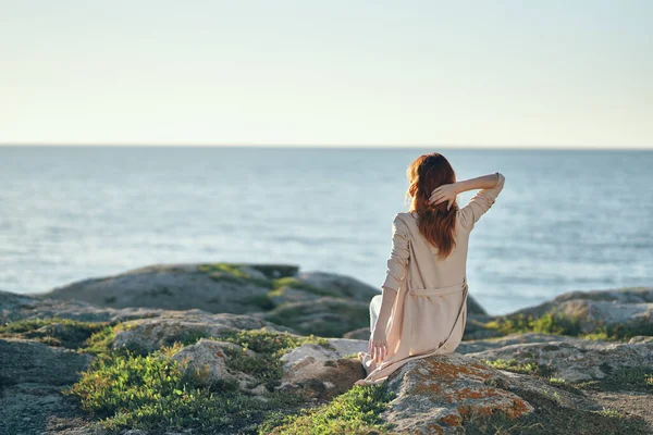 Woman in sweaters with raised up hands on a stone near the sea in the mountains — Stock Photo, Image
