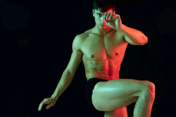 一名男子运动员用抽吸式的躯干，他的腿在黑色的背景上翘起，双手摆出姿势 — 图库照片