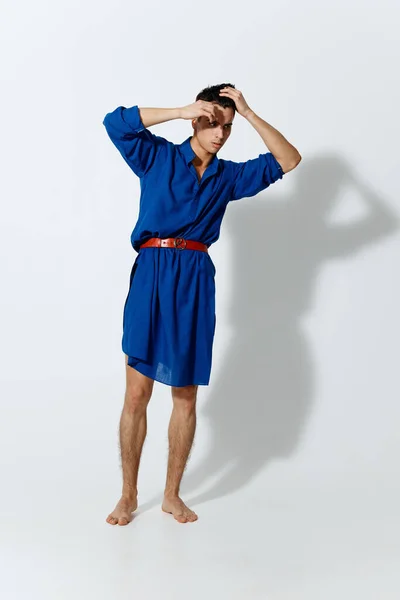 Egy vonzó férfi kék ruhában és egy pirosban, piros övvel, világos háttérrel a tarkóján tartja a kezét. — Stock Fotó