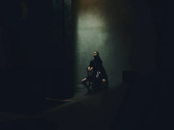 Frau Beine gespreizt sitzt auf einem Stuhl in einem dunklen Raum und fallendes Licht Innenraum Modell — Stockfoto