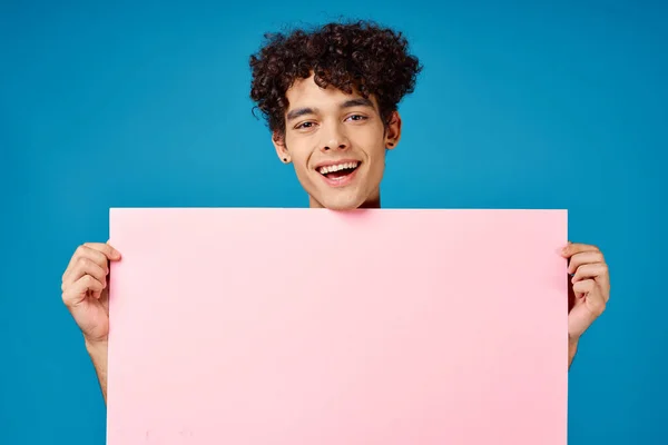 Homme aux cheveux bouclés tenant affiche rose bannière fond bleu — Photo