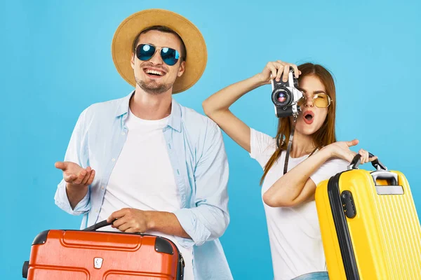Bavulları olan neşeli genç bir çift tatil gezisi için mavi arka plan — Stok fotoğraf