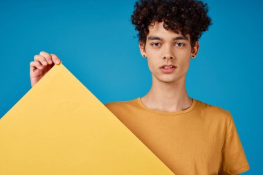 Kıvırcık saçlı, neşeli adam sarı poster modeli mavi arka plan