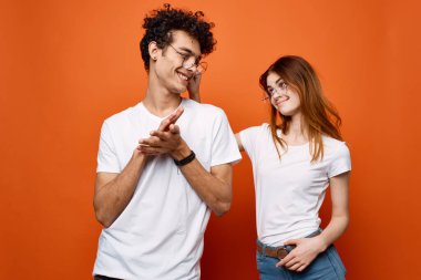 Beyaz tişörtlü ve gözlüklü genç çift eğlenceli moda turuncu arka plan